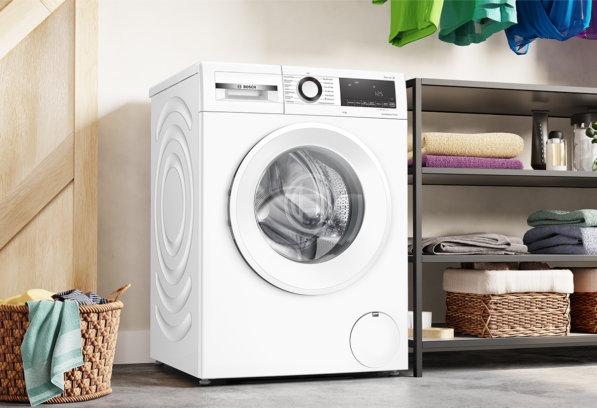 Απεικονίζεται το πλυντήριο ρούχων Bosch  WGG042L9GR, δίπλα στο οποίο βρίσκεται μία ραφιέρα με καλάθια αποθήκευσης. 
